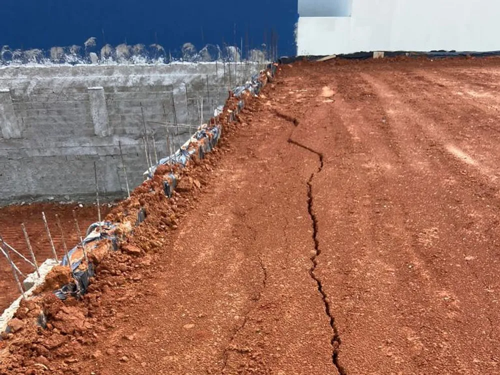Trinca longitudinal no terreno de argila, junto a um muro de arrimo com ferragens expostas
